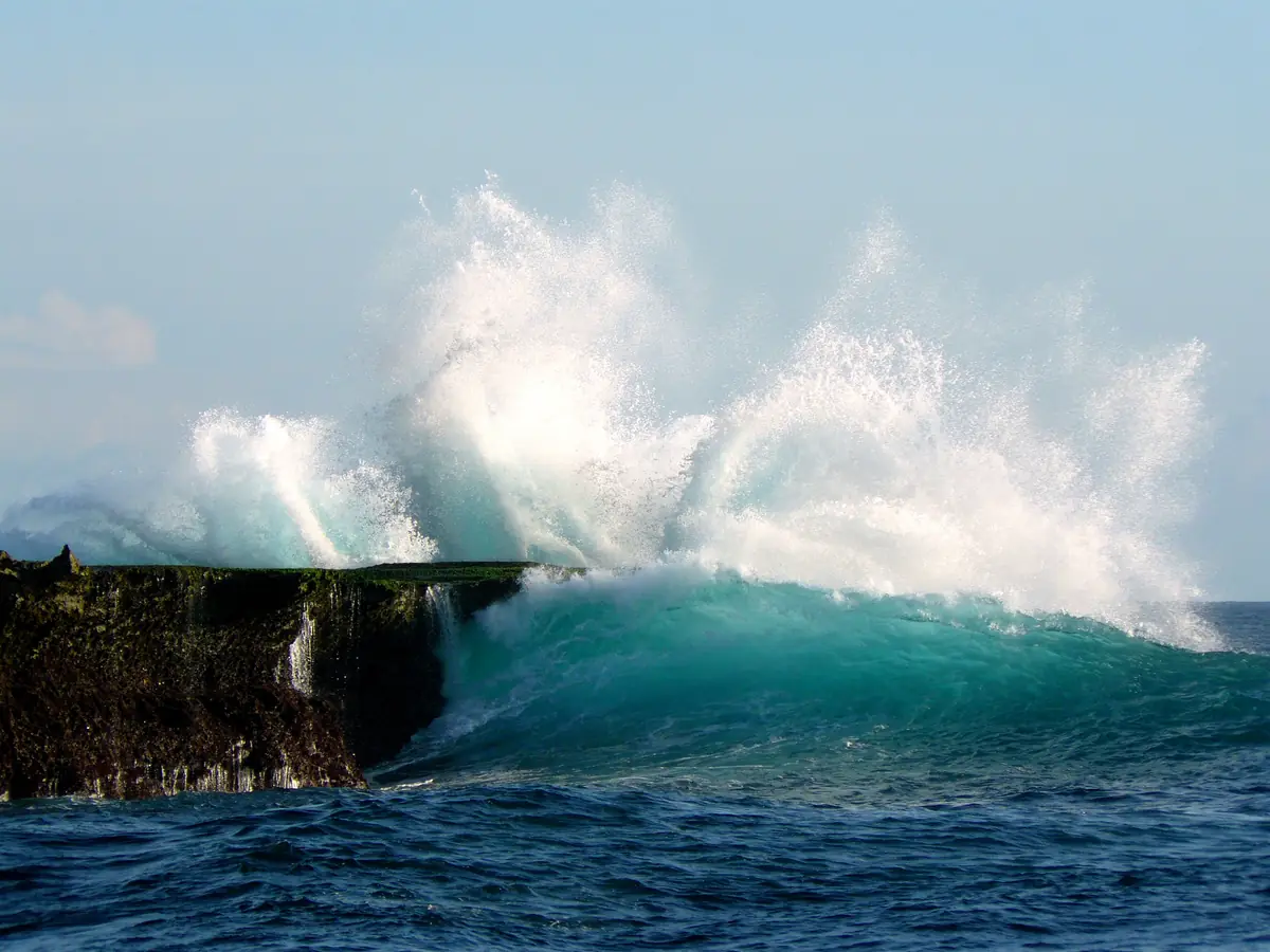A turquoise wave explodes against the rocky shore of Nusa Lembongan