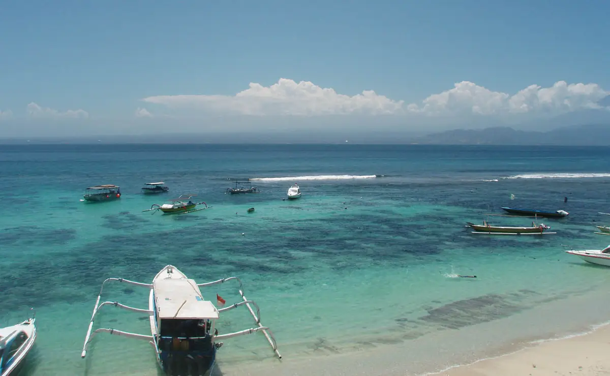 A traditional outrigger boat on the sand beside aqua water, boats moored offshore