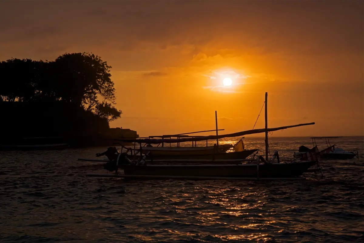 A traditional outrigger boat silhouetted on the water as the sun sets over Nusa Lembongan