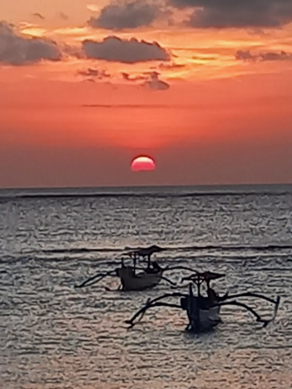 Two outrigger boats silhouetted on the sea as a red sun sets over Bali